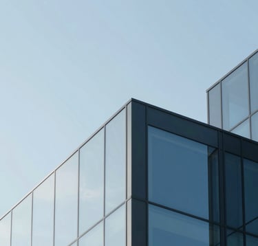 A clean, minimalist abstract image of architectural geometry with sharp lines and glass surfaces reflecting a muted blue (#658BA3) sky. The composition is sophisticated and forward-thinking, embodying professional authority.