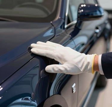 A close-up photograph of a professional curator's hand in a Soft Pearl White glove, gently touching the perfect paintwork of a Midnight Navy luxury vehicle in a high-end showroom.