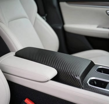 Interior shot of a high-end luxury car cockpit, focusing on the pearl white leather stitching and a minimalist center console made of deep charcoal carbon fiber. Soft, diffused lighting coming from the side.