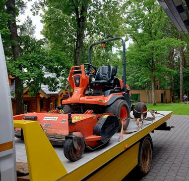 Orange Kubota ride-on lawn mower secured on a yellow flatbed truck for professional landscaping transport.