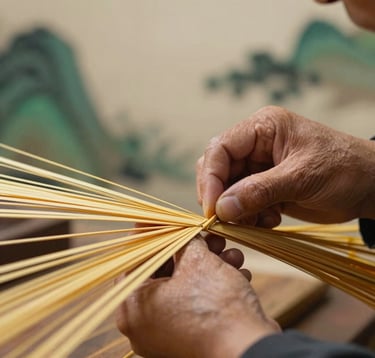 A close-up photograph of a master craftsman's hands working with golden-hued bamboo fibers. The lighting is warm and focused, highlighting the refined craftsmanship. The background is a soft ivory studio setting with subtle deep forest green accents.