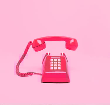 Red desktop, push-button phone with the earpiece hovering over the phone all on a pink background.
