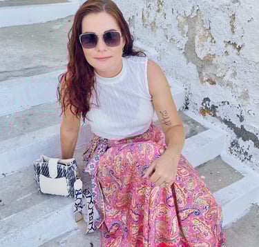 a woman in a white tank top and pink skirt sitting on stairs in Lindos village in Rhodes Greece
