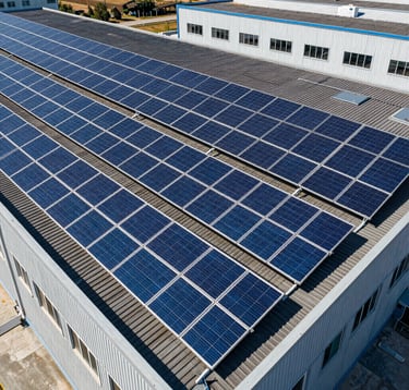 Clean aerial view of a large commercial photovoltaic system on an Italian factory roof, featuring bright electric blue solar panels against dark grey industrial tiles under sunny skies.