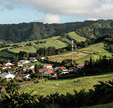 A lush green landscape of the Azores islands with a peaceful village and a communication antenna integrated into the environment, European Atlantic / Insular architecture and bright afternoon sun.