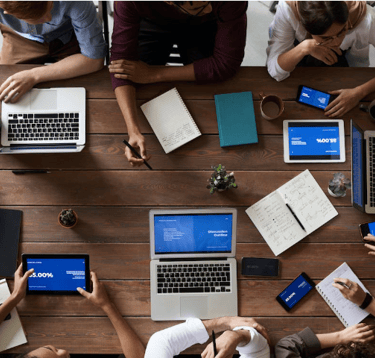 a group of people sitting around a table with laptops