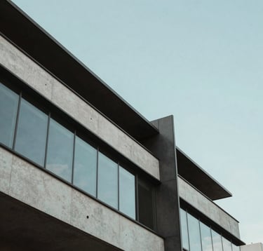 A minimalist architectural detail of a contemporary building in a Brazilian urban center. The composition focuses on clean lines and sharp angles of dark grey steel and light grey concrete. A soft baby blue sky is reflected in the polished glass surfaces, creating a serene and innovative atmosphere.