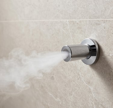 Close-up detail of a minimalist steam nozzle mounted on a light taupe marble wall. Pure white steam is gently emitting from the circular chrome head. Clean, bright, and sophisticated architectural detail within a US luxury bathroom.