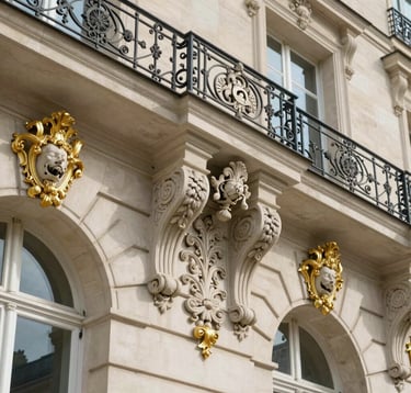 A close-up of exquisite French architectural details, featuring ornate white limestone carvings and gold-leaf accents on a classical Parisian facade, under bright, clear daylight.