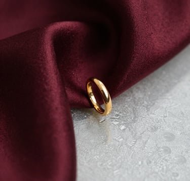 Macro photography showing the texture of deep burgundy silk and a gold jewelry piece resting near a frosted glass surface. The lighting is warm and exclusive, evoking the feeling of a private gallery in Paris. High-end lifestyle photography.