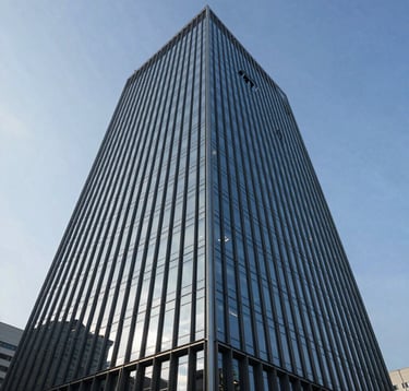 A sleek, low-angle shot of a modern glass office tower reflecting a steel blue sky. The composition emphasizes strength and scale, representing the proximity to major commercial hubs like DLF IT Park.