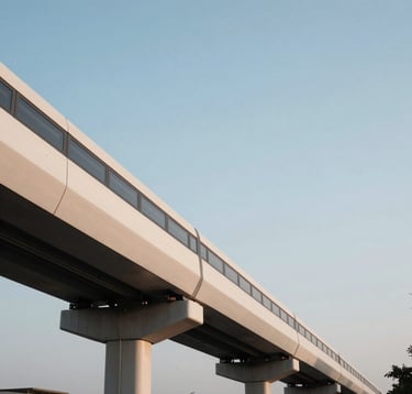 A clean, eye-level photograph of a modern elevated metro rail track in Chennai. The structure is minimalist and sleek, set against a soft white and steel blue sky at dusk.