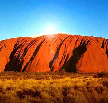 Sun glowing over Uluru, a majestic red sandstone monolith in Australia's Northern Territory.