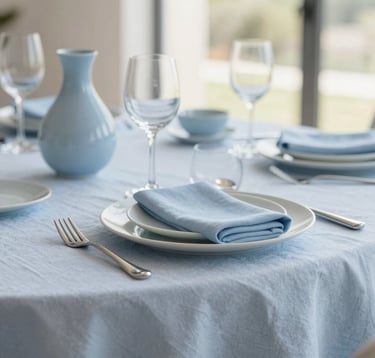 Close-up of a perfectly set dining table in a luxury Algarve villa, featuring high-end linen and minimalist ceramics. Soft morning light, very clean and sophisticated. Colors #B4C5CB and #F7F9FB dominate the scene.