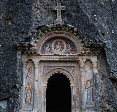 A close-up of the ancient stone entrance and intricate frescoes of the Sumela Monastery, carved directly into the dark grey cliffside of the Pontic Mountains, Eastern European / Turkish historical landmark, soft natural light.