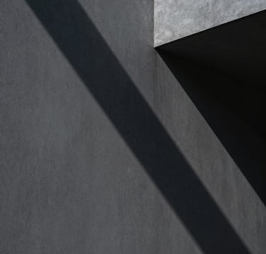 An abstract, cinematic photograph of shadows cast by sharp architectural angles on a charcoal gray wall. Minimalist and authoritative, capturing a sense of hidden depth and strategic framing. No people, North American / International Business aesthetic.