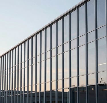 An architectural, minimalist photograph of a high-tech logistics hub in North America. The composition features clean vertical lines of silver steel and large glass panes reflecting a pale morning sky, emphasizing efficiency and modern infrastructure.