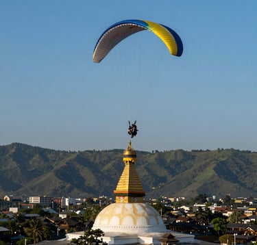 A paraglider soaring through a clear blue sky, with the golden spire of the Boudha Stupa visible far below in the valley. The sunlight highlights the rich sage green of the hills and the dark slate grey of the architectural details. Elegant and adventurous mood.