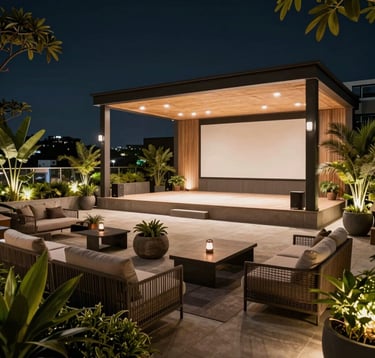 Photography of a luxury rooftop terrace garden at night with a modern open-air theatre setup. Soft ambient lighting, contemporary lounge furniture, and lush potted plants. Elegant South Asian / Indian atmosphere reflecting high-end residential amenities.