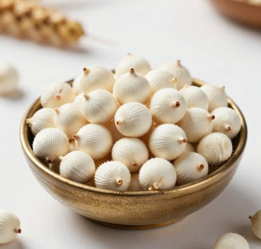A high-quality macro photograph of white, puffed Makhana seeds beautifully arranged in a traditional South Asian / Indian bowl. The background is a clean, pearl white kitchen surface with soft natural lighting and a hint of harvest gold.