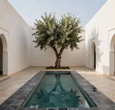 A wide angle shot of a minimalist North African / Moroccan courtyard garden. A narrow reflecting pool is lined with dark charcoal tiles. Soft off-white walls surround the space, and a single olive tree stands as a focal point. Bright, natural daylight creates clean lines and a peaceful, premium atmosphere.