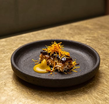 A high-end gastronomic presentation in a modern North African / Moroccan restaurant. A gourmet dish is plated on dark charcoal stoneware, garnished with saffron-colored elements that match a muted gold background. Soft side-lighting emphasizes the culinary artistry and luxury setting.