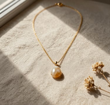 An elegant flat lay photography of jewelry components on a natural sandy beige linen background. A delicate golden necklace with a tiny shell pendant, semi-precious stones in soft cream and warm tan hues, and dried flowers. Soft light from a side window in Rennes, Western Europe / Brittany, France, casting long, gentle shadows.