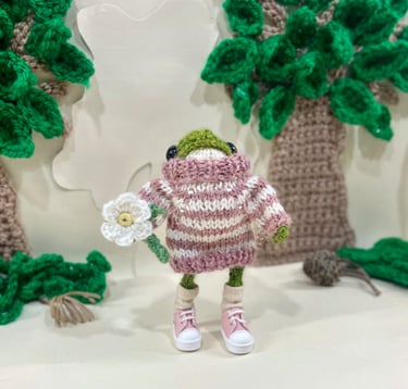 a froggy frog wearing a striped jumper holding a crochet flower