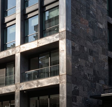 A close-up architectural shot of a contemporary building facade in Rosario, showcasing high-quality materials like brushed steel, glass, and dark stone. The style is sophisticated and urban, reflecting professional expertise. Sunlight creates sharp, clean shadows in a South American city setting.
