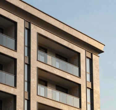Close-up photography of a modern luxury apartment complex exterior. The architecture features clean, minimal lines, large glass surfaces, and textured warm beige stone cladding. The scene is shot during the golden hour, with soft light highlighting the premium finish of the materials.