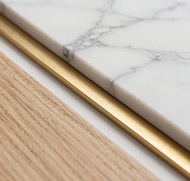 Close-up macro photography of high-end architectural materials. A combination of polished white marble with gray veins, a sample of warm beige oak wood, and a brushed polished gold metal element, arranged in a minimalist, clean composition.