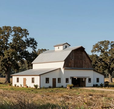 Wide-angle photography of a modern rustic North American / US farm house and barn. The structures feature soft off-white painted wood and deep dark brown trim, set against a backdrop of ancient oak trees and vast, well-maintained pastures under a clear blue sky.