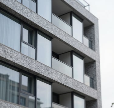 A detail shot of premium architectural materials: polished grey granite and clean glass panels of a modern apartment building in Bellandur. The shot is sharp and sophisticated, highlighting quality and physical integrity.