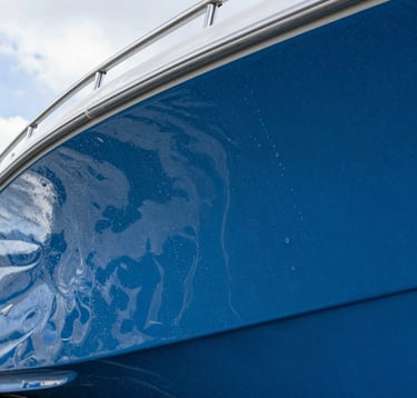 A high-detail photograph of water beading perfectly on a ceramic-coated blue boat hull. The reflections of the Florida sky are visible in the paint. Meticulous focus on the glossy, hydrophobic surface.