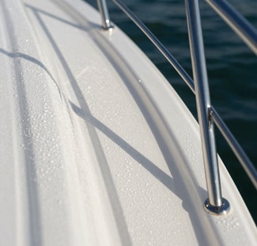 Macro photography of a yacht's surface after detailing. Water beads perfectly on the polished white surface. Silver accents of the railing glisten in the bright Florida sunlight. Sharp focus on the glossy, mirror-like finish.