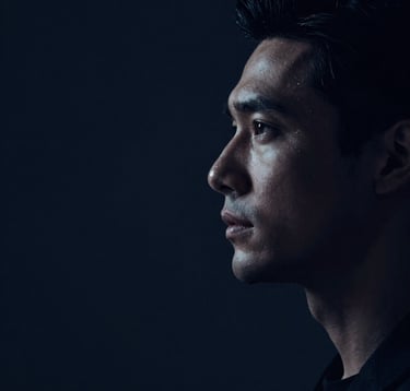 A minimalist, low-key portrait of a man in shadows, only showing the profile and a focused gaze. Cinematic lighting accentuates a sharp jawline and calm expression. Colors are deep navy (#0C1E38) and subtle silver highlights.
