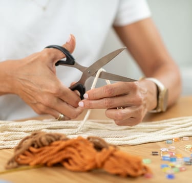 persona cortando cuerdas para macrame con tijeras, sobre una mesa de madera
