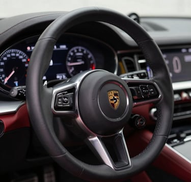Close-up macro shot of a luxurious car interior, showing the premium leather steering wheel and sleek digital dashboard. Red accents, ambient cabin lighting, highly detailed.