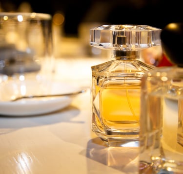 A glass perfume bottle with amber liquid and a faceted cap sits on a reflective surface