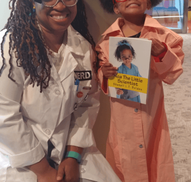Shenell poses for a pic kneeling in her lab coat with a mini scientist holding her book