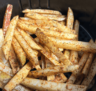Seasoned uncooked fries inside an air fryer pan.
