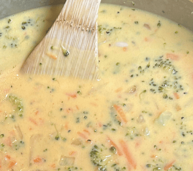 Broccoli Cheddar Soup in a pot with a wooden spoon sitting there.