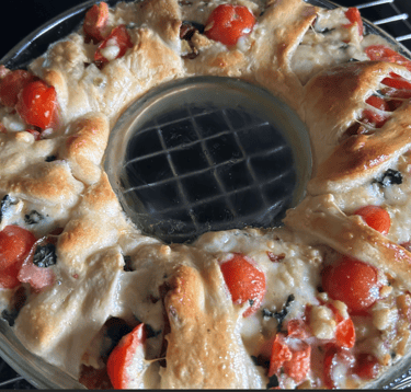Ring of Goodness dish just out of oven. Breaded top with tomatoes, cheese and veggies sticking out the top.
