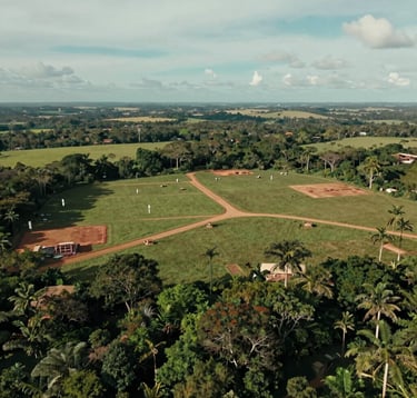 A wide, cinematic drone shot of a pristine, large plot of land ready for development in a South American / Brazilian landscape, lush greenery contrasting with early construction markers, professional photography, muted teal and light grayish blue sky.
