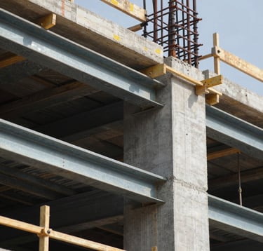 An architectural detail shot emphasizing structural strength. High-quality steel frames and reinforced concrete meet with surgical precision. The lighting highlights the geometric perfection and the safety-first approach of the construction site, using brand colors.