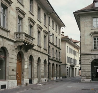 Clean, architectural view of a classic luxury street in Geneva's old town. Limestone buildings, elegant details, minimalist frame, soft daylight, quiet luxury vibe. European Swiss context.