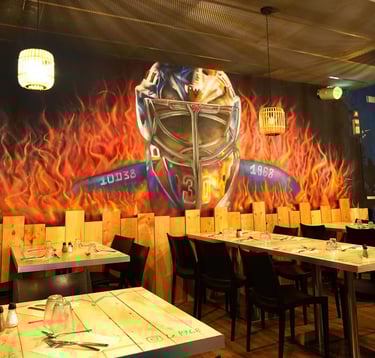 Modern restaurant dining room featuring a mural of a hockey goalie mask and flames.