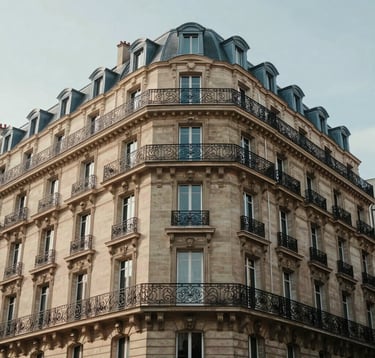 Exterior shot of a classic Haussmannian apartment building in a prestigious Paris neighborhood. The architecture is detailed with stone carvings and wrought iron balconies, captured in soft morning light, representing premium real estate.