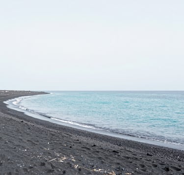 A minimalist landscape of a secluded beach with dark volcanic sand and clear turquoise water. The composition is clean and tranquil, using a palette of soft whites (#F7F9FA) and light blues (#A8C9CF). Very elegant and peaceful mood.