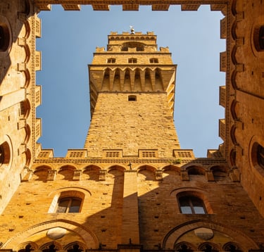 Low angle view of the Arnolfo Tower at Palazzo Vecchio in Florence, Italy, framed by a stone courtyard.